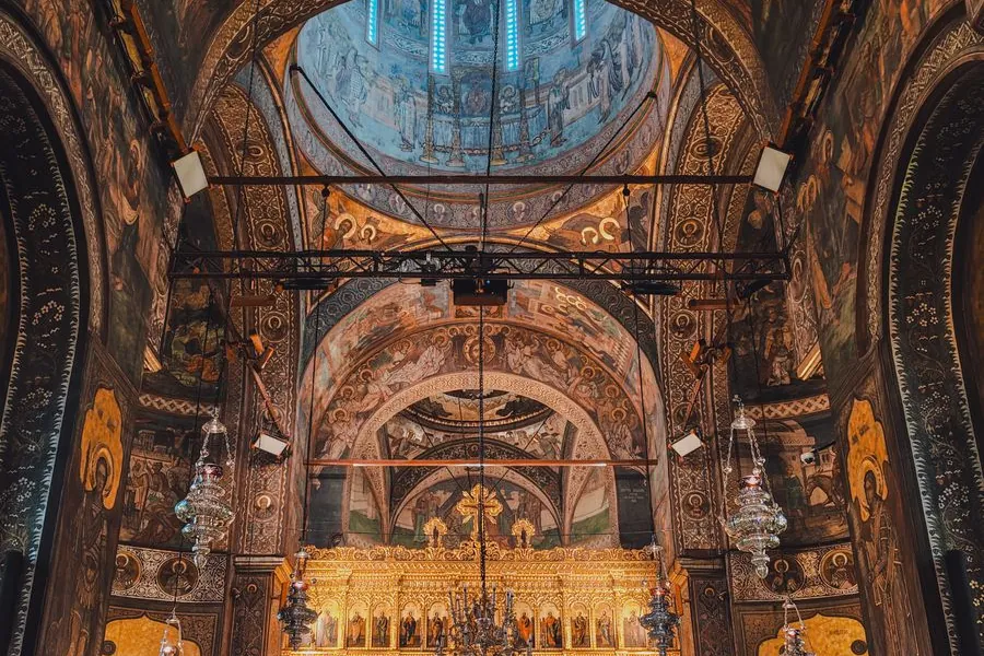 The painted interior of an Orthodox church, with a gilded iconostasis below a frescoed dome.